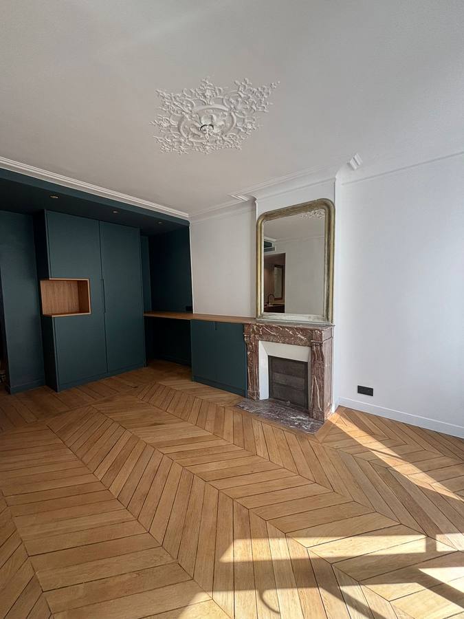 Séjour haussmannien avec parquet chevron, rosace au plafond, cheminée en marbre et rangements bleu-vert sur mesure