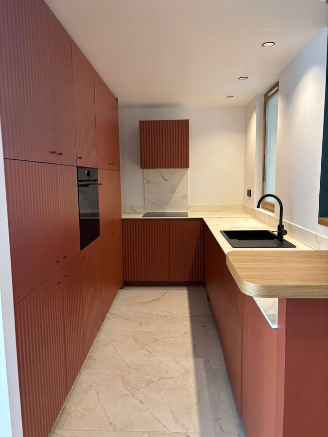 Cuisine aux façades cannelées terracotta, plan de travail effet marbre et retour bar en chêne